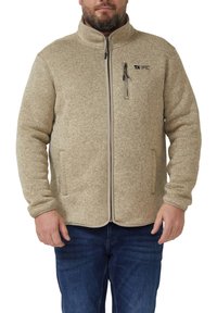 Veste en polaire beige avec un col montant, une fermeture éclair frontale, des poches latérales et une petite poche sur la poitrine. Tissu texturé et confortable.