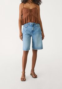 Top marrón con encaje y tirantes, combinado con shorts de mezclilla azul claro de talle alto. Sandalias marrones completan el conjunto.