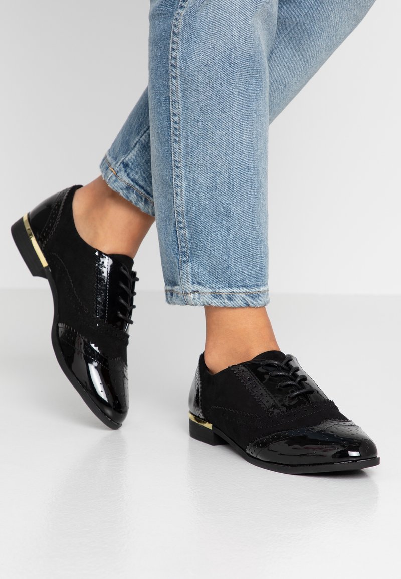 Oxfords noirs avec une combinaison de textures en cuir verni et en daim, des détails en brogue et un accent doré sur le talon. Semelle en caoutchouc.