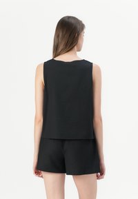 Svart utenermed topp med rund hals og løs passform, laget av et glatt stoff. Kombinert med matchende svarte shorts.