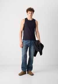 Top din bumbac de marină cu dungi, blugi drepti de un albastru deschis, pantofi slip-on maro, ținând o jachetă neagră; design simplu și croială casual.