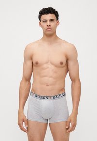 Boxeri pentru bărbați de culoare gri, cu un brâu de nuanță navy, care are logo-ul "GUESS". Materialul pare a fi moale, cu o Textură netedă. Design clasic.