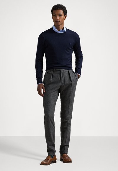 Pull en tricot marine, chemise col bleu en dessous, pantalon gris plissé, et mocassins en cuir marron. Tissu texturé, coupe ajustée.
