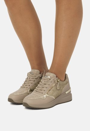 Zapatilla beige con acentos metálicos, parte superior de malla, cordones en la parte delantera y cremalleras en los laterales. Cuenta con una suela gruesa y tejido texturizado para mayor agarre.