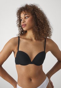 Svart formet push-up BH med tynne justerbare stropper. Glatt stoffoverflate og rund design, med subtile sømmer for støtte.