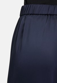 Granatowe spodnie z wysokim stanem i elastycznym paskiem w talii, wykonane z miękkiego materiału, z delikatnymi plisami, zaprezentowane w zbliżeniu.