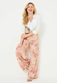 Lightweight, flowy pink pants with floral patterns, paired with a white button-up shirt and a small beige handbag. Strappy sandals complete the look.