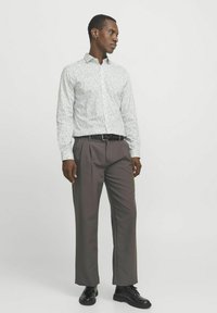 Camisa blanca con estampado floral, pantalones de tiro alto marrones, cinturón negro y zapatos negros. Diseño ajustado con mangas largas.