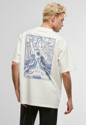 Kremfarget oversized t-skjorte med trykk av en blå donut og abstrakte design på baksiden. Laget av bomull, avslappet passform.