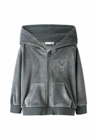 Haut à capuche grise en velours avec une broderie en forme de cœur à l'avant, deux poches avant et une grande capuche. Poignets et ourlet côtelés.