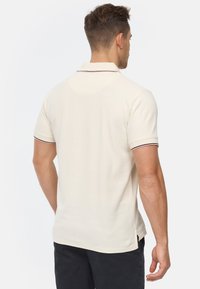 Polohemd in Creme mit klassischem Kragen und kurzen Ärmeln, versehen mit dunkler Einfassung am Kragen und an den Ärmeln. Weicher, strukturierter Stoff.