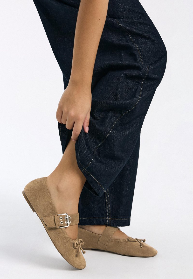 Beige ruskind ballet flats med rundet tå, en sløjfedetalje og en sølvspænde, kombineret med mørke denim bukser med vide ben.