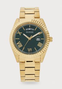 Montre dorée avec un cadran vert, des chiffres romains et une fenêtre de date. Présente une lunette texturée et cannelée ainsi qu'un bracelet en acier inoxydable.