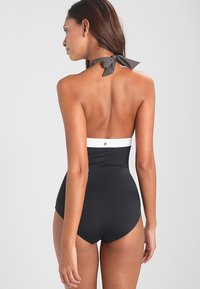 Maillot de bain une pièce noir avec une bande blanche en haut et un lien gris au cou. Tissu lisse, forme ajustée et détails minimaux au dos.