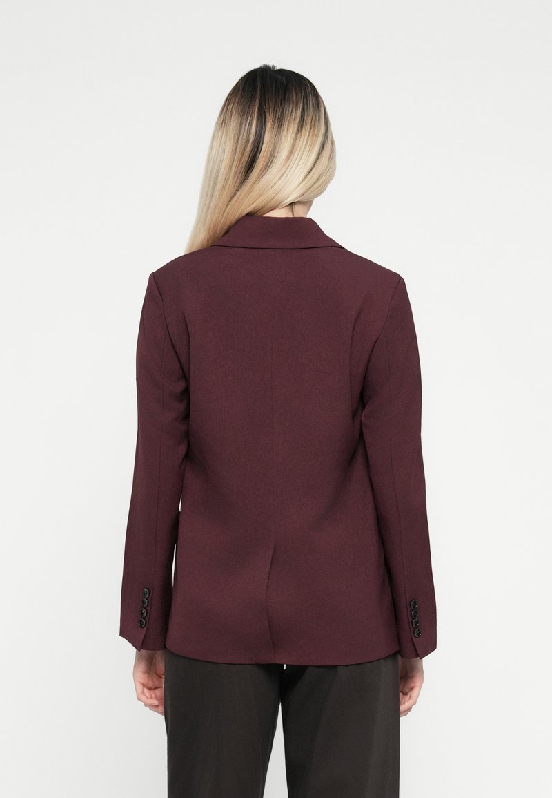 Blazer bordeaux con design a una sola petto, colletto a punte e maniche lunghe con dettagli a bottoni. Tessuto liscio e vestibilità sartoriale.