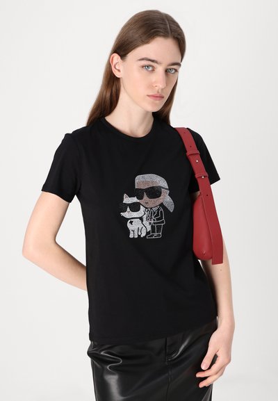 T-shirt noir avec un graphique en strass de deux personnages portant des lunettes de soleil, à manches courtes et coupe classique. Texture de tissu uni.