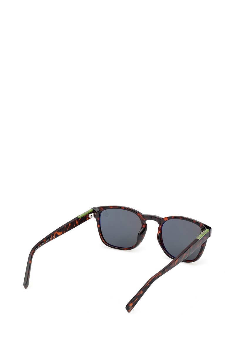 Lunettes de soleil en écaille de tortue avec des verres foncés et un motif distinct. Présente des accents verts sur les branches et un design de monture rectangulaire.