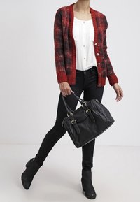 Cárdigan a cuadros en rojo y negro con botones, blusa blanca, jeans negros ajustados, bolsa negra y botines. Texturas suaves, diseño clásico.
