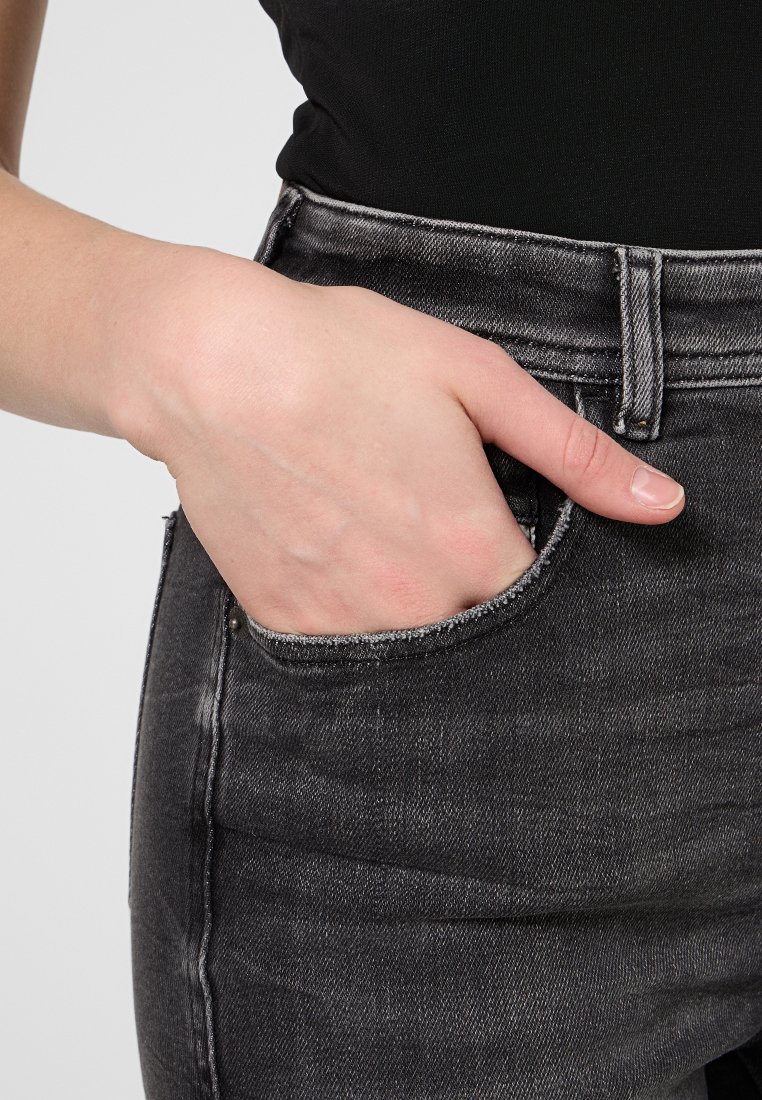 Schwarze Denim-Jeans mit einer ausgefransten Tasche, hoher Taille und engem Schnitt. Der Stoff zeigt ein verblasstes, strukturiertes Muster mit sichtbaren Nähten.