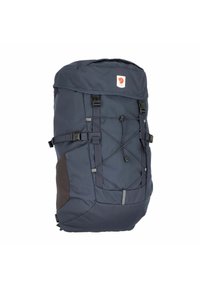 Mochila azul marino con tapa superior, correas ajustables, bolsillos laterales, cordón elástico en la parte delantera y acentos grises. Diseño de tela duradera.