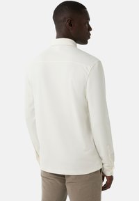 Langsleeve shirt in off-white stof met een gladde textuur, met een klassieke kraag en knoopmanchetten, weergegeven vanaf de achterkant.