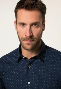 Camicia blu navy con bottoni e pois bianchi, dotata di una tasca sul petto, colletto standard e tessuto strutturato.