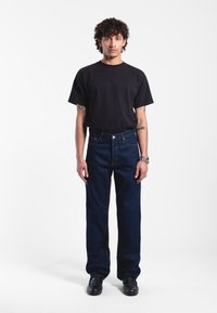 Dark blue denim jeans with a straight-leg cut, paired with a black short-sleeve t-shirt. Buttons and stitching are visible on the jeans.