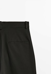 Svarta byxor i ett slätt, texturerat tyg, med en platt midja, bälteshällor och en enda bakficka utan synlig hårdvara.