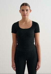 Top negro de canalé ajustado con escote redondo y manga corta, combinado con leggings de tiro alto a juego. Textura suave, diseño minimalista.