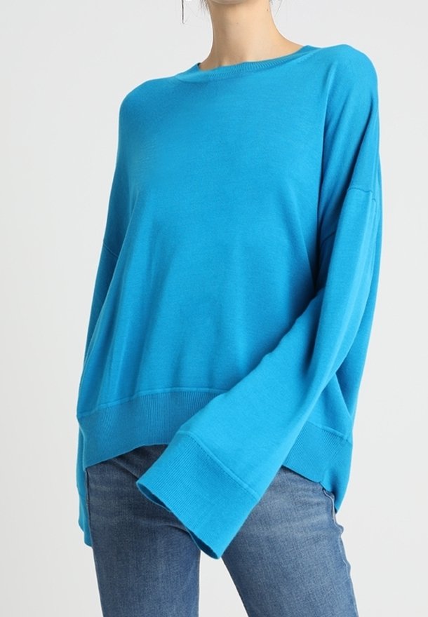 Übergroßer türkisfarbener Pullover mit langen Ärmeln und geripptem Saum. Weiche Textur, Rundhalsausschnitt und lockere Passform, kombiniert mit Denim-Jeans.