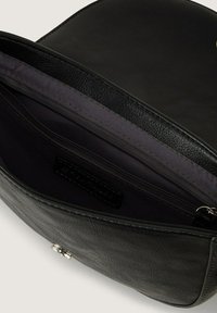 Intérieur d'un sac en cuir noir avec un revêtement en tissu foncé, comportant une petite poche zippée et une étiquette de marque. Texture lisse, forme compacte.