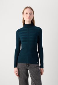 Mørk teal ullgenser med høy krage, med strukturert ribbing og slank passform, med horisontale striper på brystet og lange ermer.