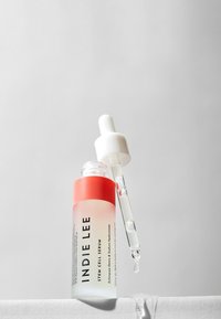 Klar glassflaske med gradientfarge fra rosa til gjennomsiktig; hvit dråpehette; merket "INDIE LEE STEM CELL SERUM."