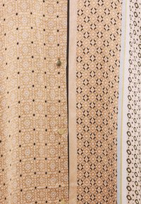 Skjorta med knappar i beige och brunt blommönster, med kontrasterande svarta och vita detaljer samt knappar i guldton framtill.