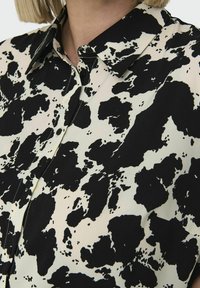 Sorte og hvide mønstrede skjorte med krave, knappelukning og en glat stoftekstur med abstrakt pletdesign.
