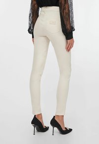 Beiget korkeavyötäröiset kapealahkeiset farkut, joissa takataskut, yhdistetty mustaan pitsipaitaan ja mustiin korkokengänn, joissa on kultaiset yksityiskohdat.