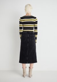 Jupe midi en denim noir avec poches arrière, associée à un top à rayures noir et olive en maille à manches longues. Portée avec des bottines beige clair à la cheville.