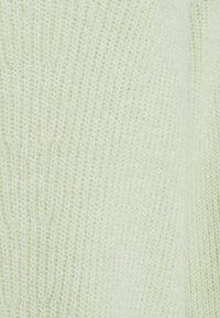 Tissu tricoté doux et vert clair avec un motif côtelé présentant de petites mailles uniformément espacées et une couture verticale sur le côté droit.
