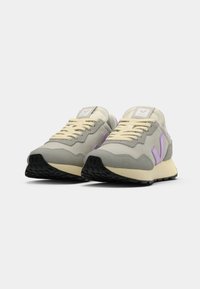 Tenis em malha cinza com detalhes em bege, logótipo roxo, biqueira redonda, língua texturizada e sola de borracha preta. Cadarços em bege claro.