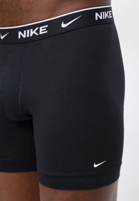 Μαύρα μπόξερ της Nike με λευκό λογότυπο στη μέση και στο κάτω αριστερό πόδι, φορεμένα στη λεκάνη και τους μηρούς ενός ατόμου.