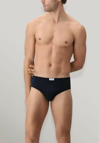 Slips da nuoto neri con una texture morbida e liscia, caratterizzati da una toppa con logo sulla vita. Design classico con una forma aderente.