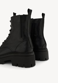 Melnas ādas potīšu zābakus ar masīvu zoli, kas ir ar auklām un sānu rāvējslēdzēju, gludiem virsmas tekstūru un minimālām šuvju detaļām.