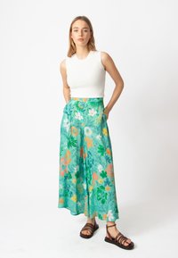 Lichte teal wijde broek met bloemenprint, voorzien van tinten groen, oranje en witte bloemen. Lichtgewicht stof met zijzakken.
