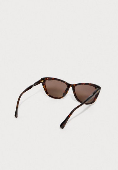 Ochelari de soare cu rame de testoasă, cu formă de ochi de pisică, lentile de culoare maro și brațe negre elegante. Prezintă un brand discret pe interiorul tempelului.