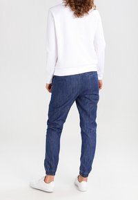 Sweatshirt blanc texturé avec un col rond, associé à un pantalon de jogging bleu fuselé avec des poignets élastiques et des poches arrière. Baskets blanches.