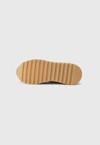 Semelle de chaussure en caoutchouc beige texturé avec des rainures horizontales pour une meilleure adhérence et traction, présentant un bout arrondi et un talon plat.