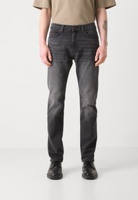 Dark gray denim jeans with a straight cut, five-pocket design, faded texture, and button closure. Worn with a beige T-shirt and black shoes.