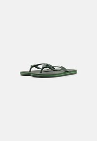 Grønne flip-flops med teksturerte gummiremmer og såler. Har en kontrasterende grønn aksent langs kanten. Lett og fleksibel design.