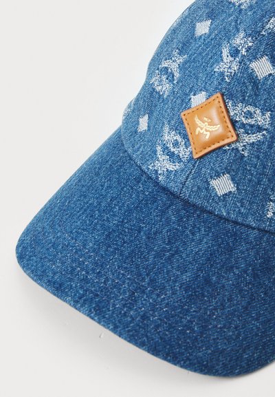Denim beisbola cepure ar strukturētu kroni, zils tonis, dekoratīvi balti raksti un brūna ādas plāksne ar iepresētu logo priekšpusē.
