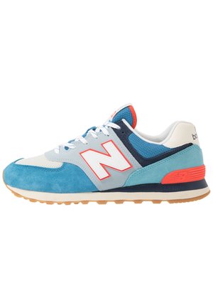 Niebieski, biały i szary sportowy but z białymi sznurowadłami, panelami z zamszu i siateczki, czerwonymi akcentami i teksturowaną gumową podeszwą.